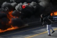Seorang demonstran melempar kerucut lalu lintas saat api menyala selama protes terhadap razia imigrasi federal di pusat kota Los Angeles, California, AS, Minggu (8/6/2025). Foto: Daniel Cole/REUTERS 