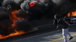 Seorang demonstran melempar kerucut lalu lintas saat api menyala selama protes terhadap razia imigrasi federal di pusat kota Los Angeles, California, AS, Minggu (8/6/2025). Foto: Daniel Cole/REUTERS 